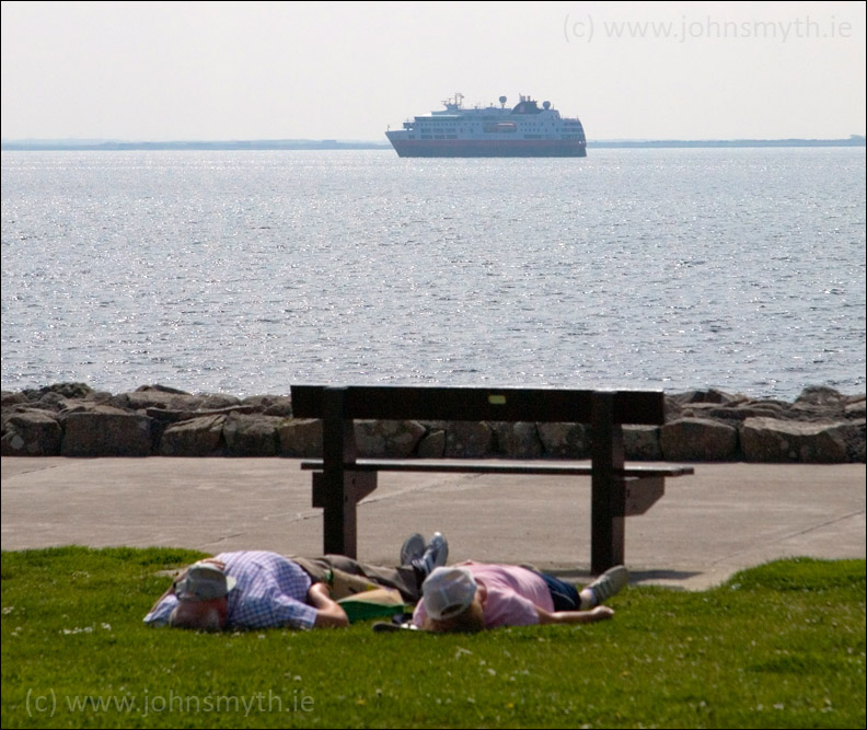 Sunbathers on Salthill Prom with cruise ship in the background in Galway Bay